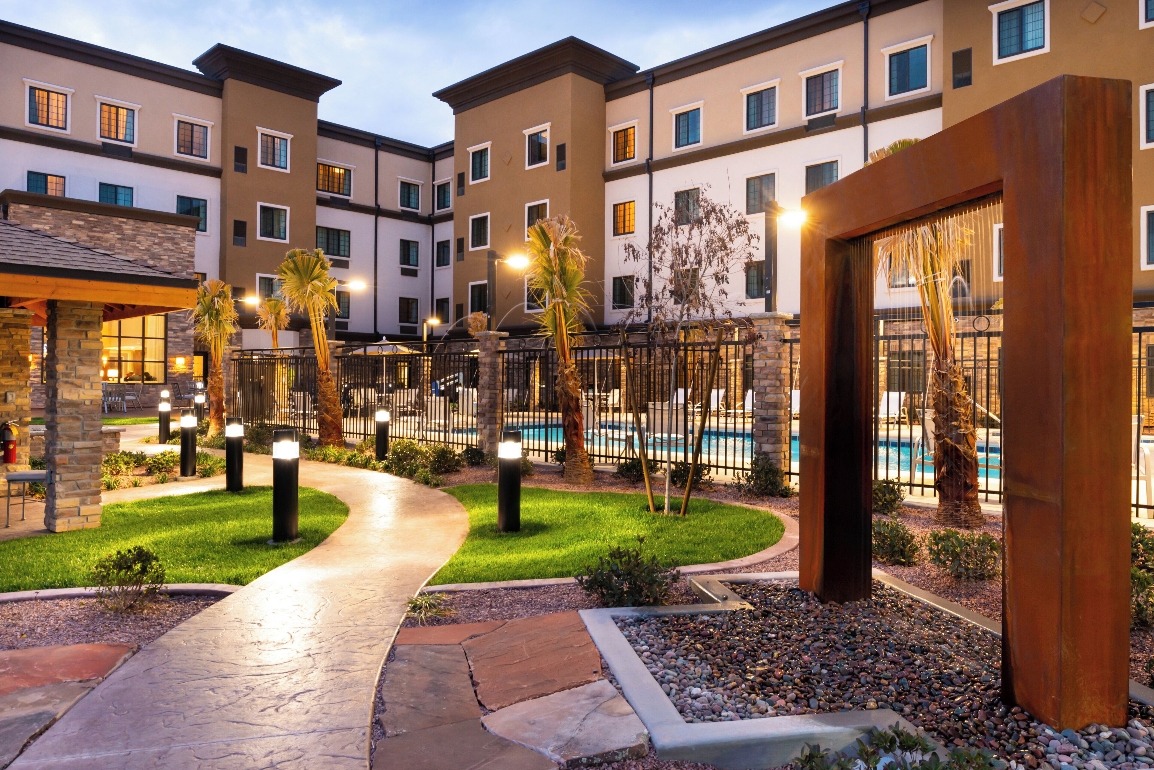 A hotel courtyard with a swimming pool, palm trees, and a stone pathway.