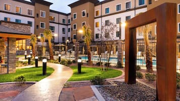 A hotel courtyard with a swimming pool, palm trees, and a stone pathway.