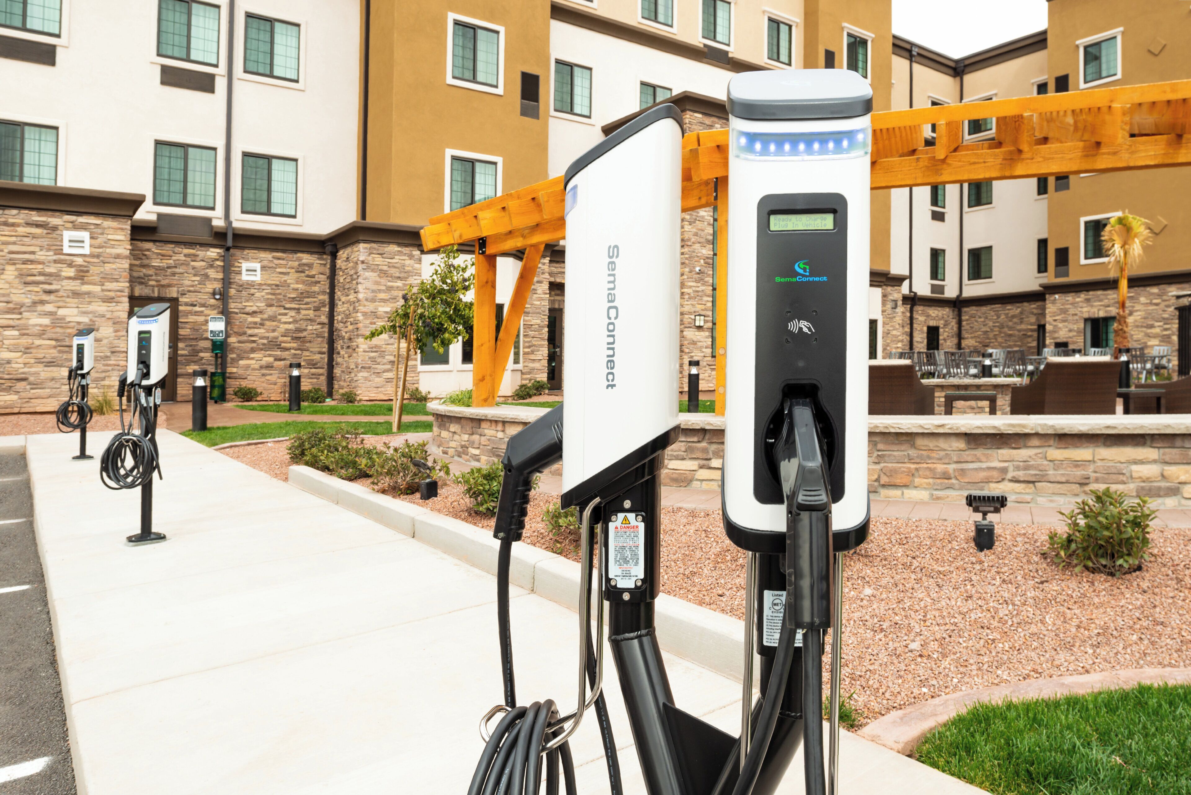 A parking area with electric vehicle charging stations, a stone building, and a wooden pergola.