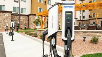 Un espace de stationnement équipé de bornes de recharge pour véhicules électriques, un bâtiment en pierre et une pergola en bois.