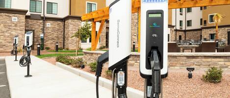 A parking area with electric vehicle charging stations, a stone building, and a wooden pergola.