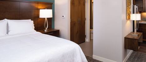A hotel room with a bed, nightstands, a lamp, a door, and a painting on the wall.