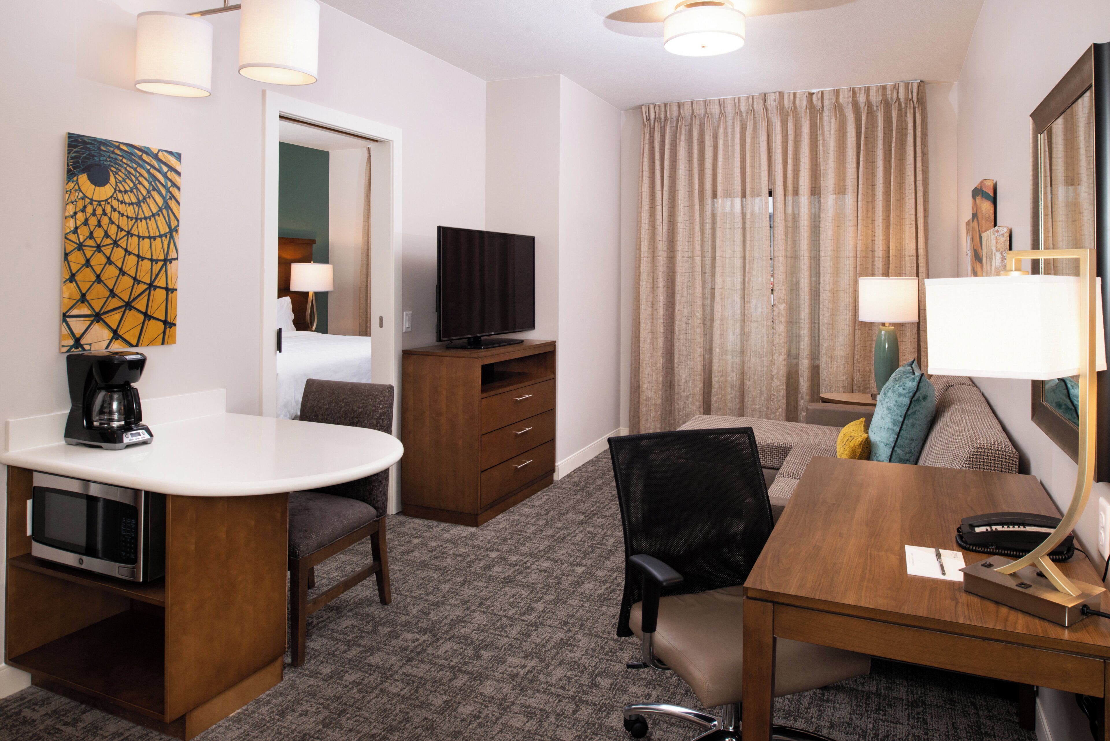 A hotel room with a bed, a desk, a chair, a television, a coffee maker, and a painting on the wall.