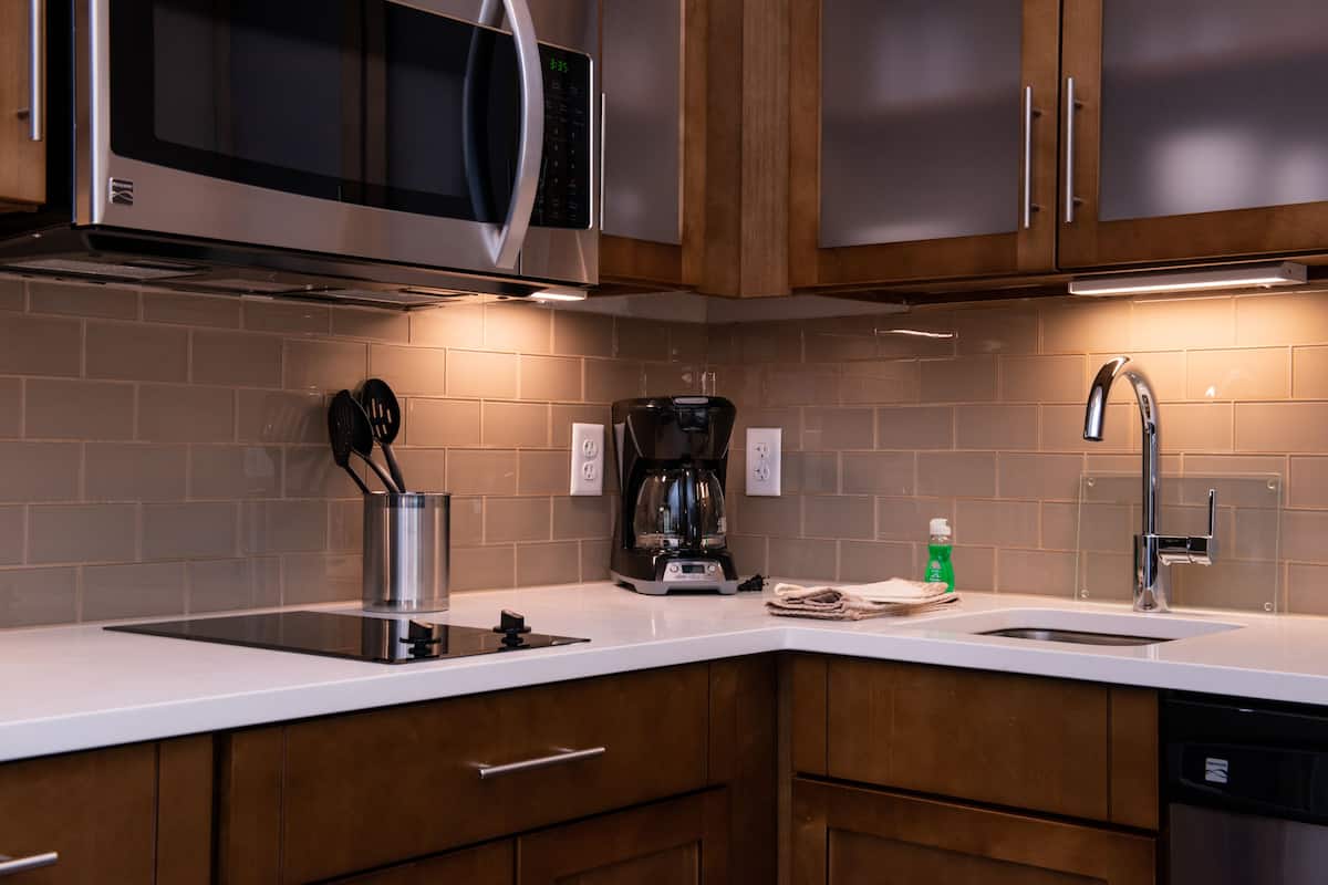 Una cocina moderna con electrodomésticos de acero inoxidable, armarios de madera y encimera blanca.