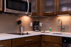 Una cocina moderna con electrodomésticos de acero inoxidable, armarios de madera y encimera blanca.