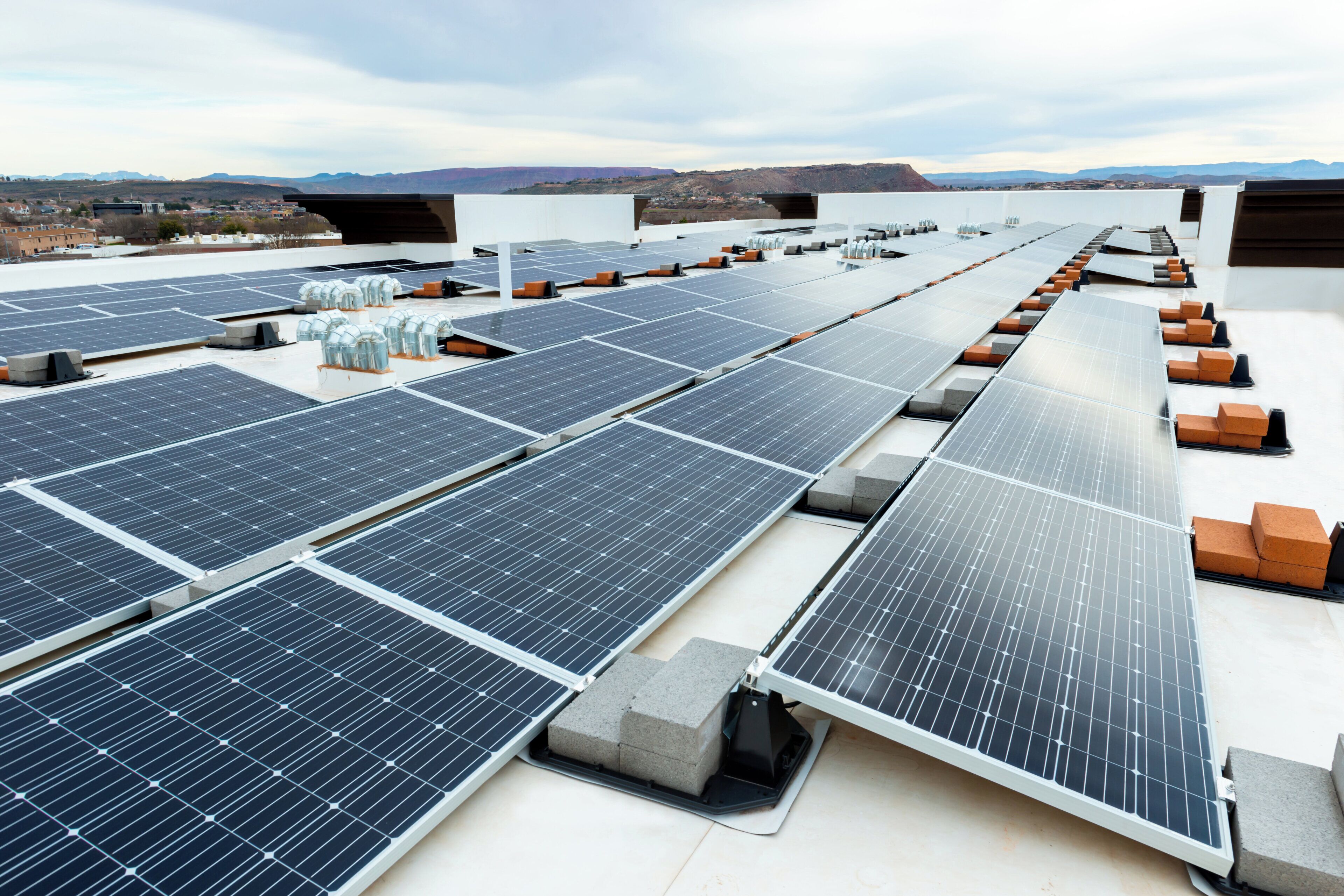 Paneles solares dispuestos en una azotea plana, con cielo despejado y montañas lejanas al fondo.