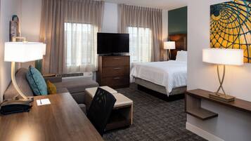 A hotel room with a bed, a desk, a chair, a television, and a painting on the wall.