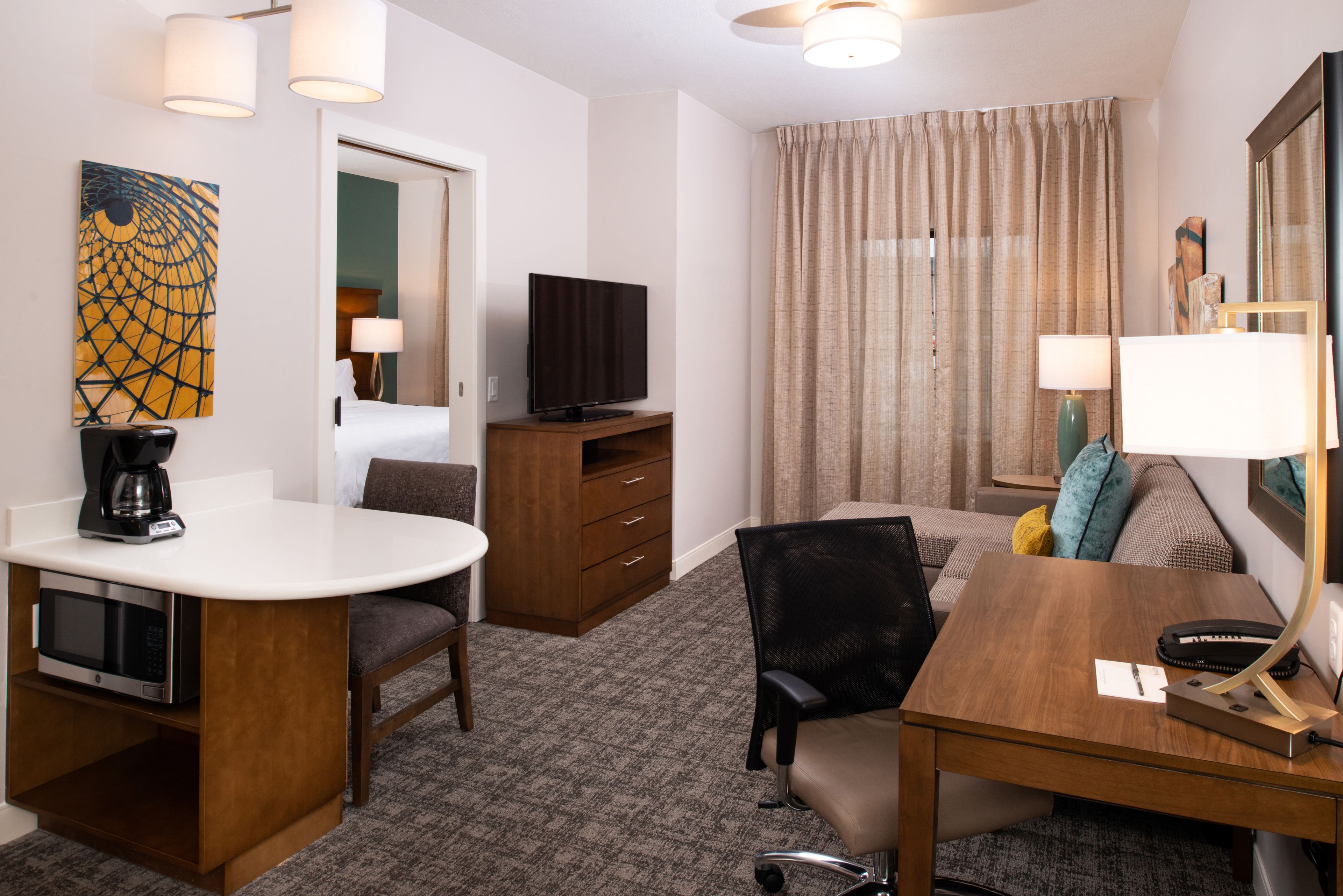 A hotel room with a bed, a desk with a chair, a television, a coffee maker, and a lamp.