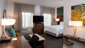 Quarto de hotel com uma cama, uma escrivaninha, uma televisão, um abajur e um quadro na parede.