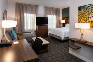 A hotel room with a bed, a desk, a television, a lamp, and a painting on the wall.
