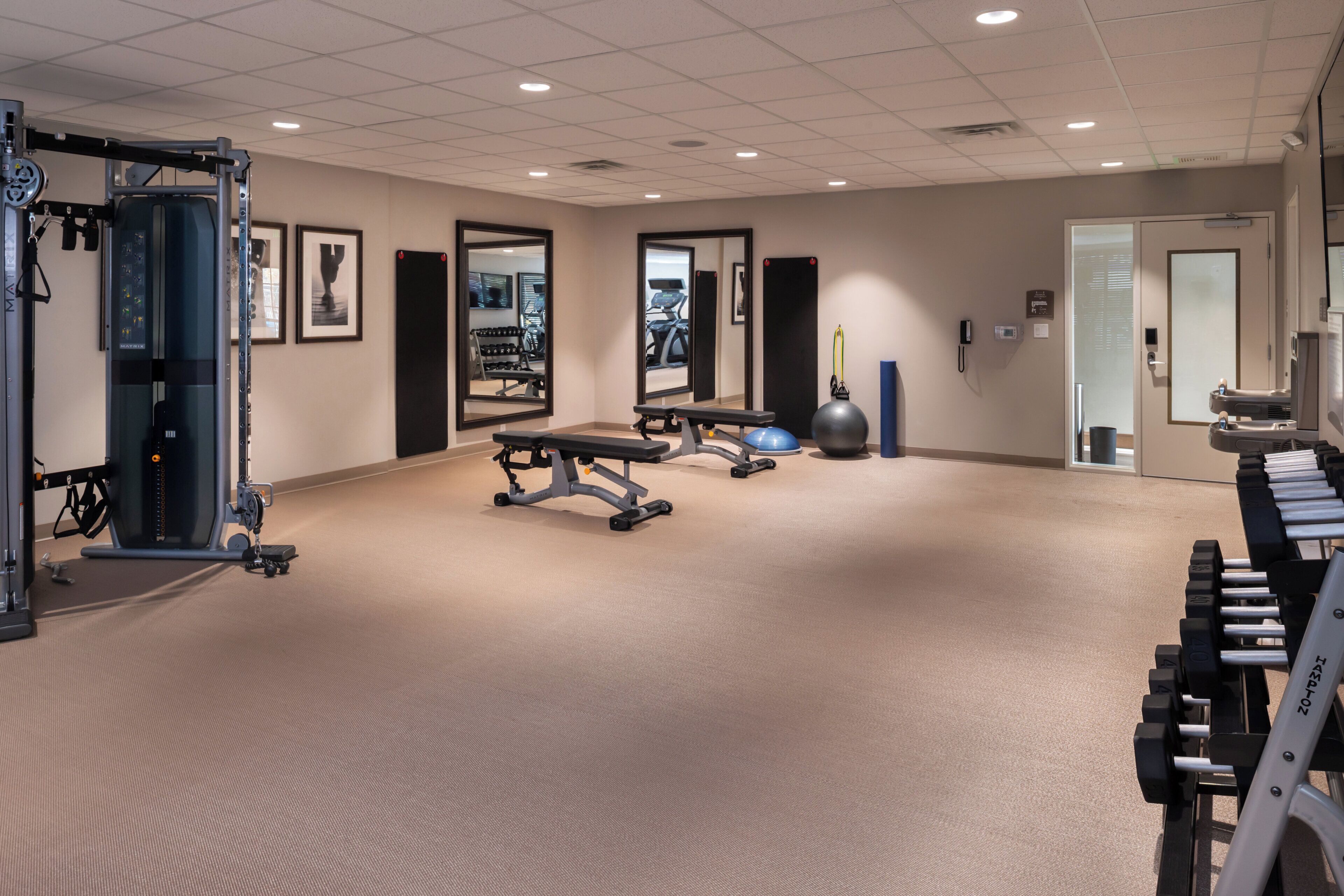 Een sportschool met trainingsapparatuur, spiegels en een vloerbedekking.