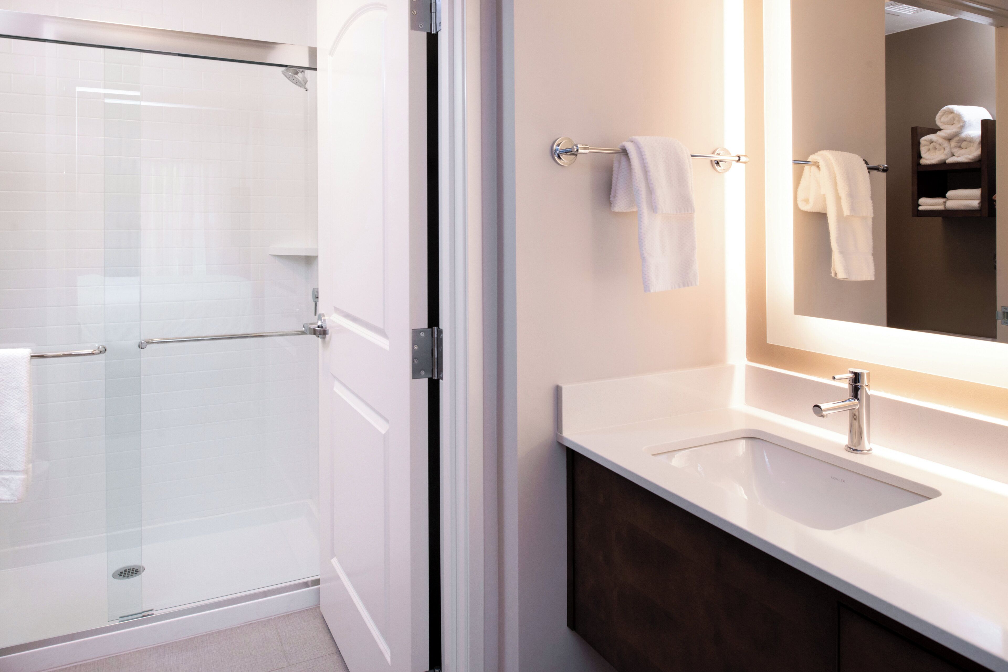 A modern bathroom with a glass shower enclosure, a white sink, and a mirror with a towel rack.