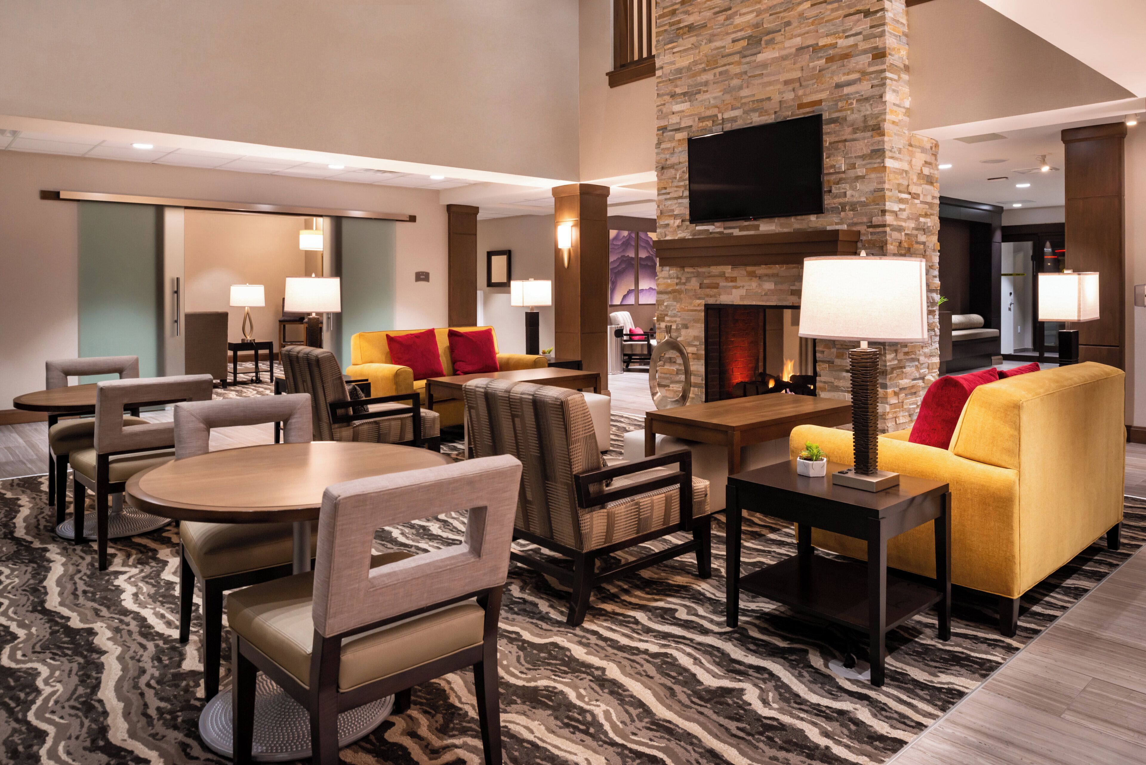 A hotel lobby with a stone fireplace, seating areas, and a flat-screen TV mounted on the wall.