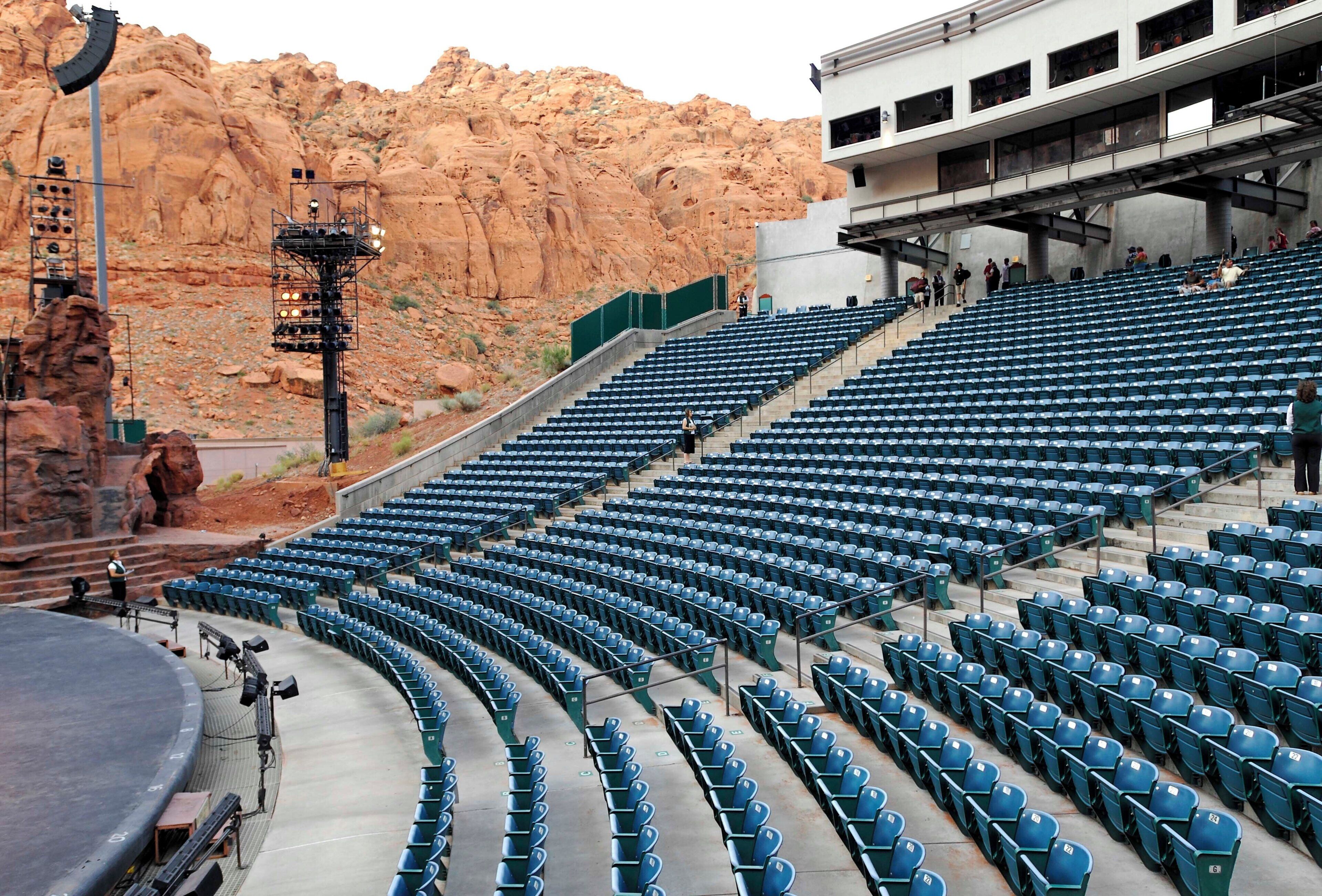 A stadium with blue seating arranged in a semi-circular pattern, a stage area, and a desert landscape in the background.