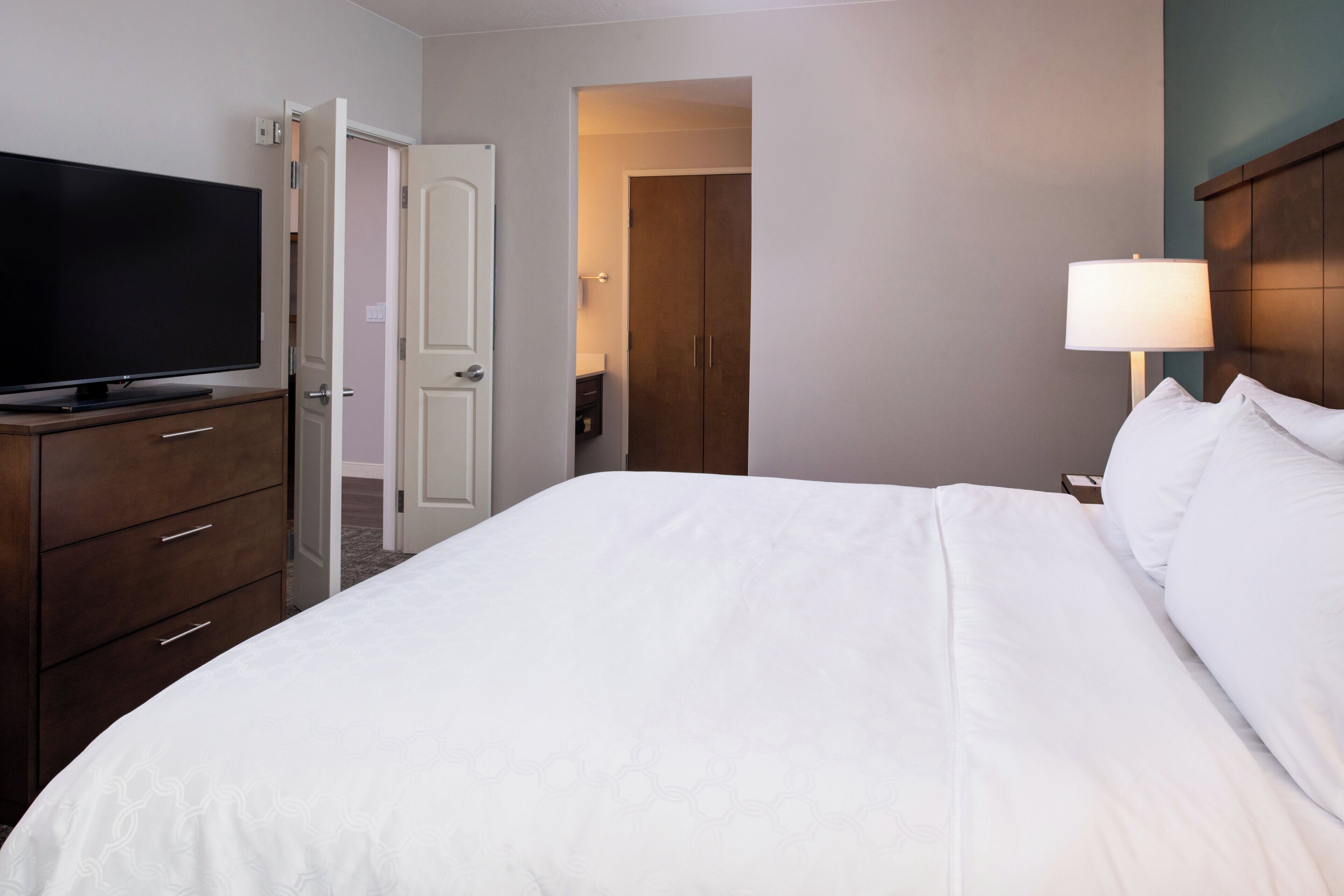 Une chambre d’hôtel avec un lit, un téléviseur posé sur une commode, une lampe et une porte donnant sur une autre pièce.