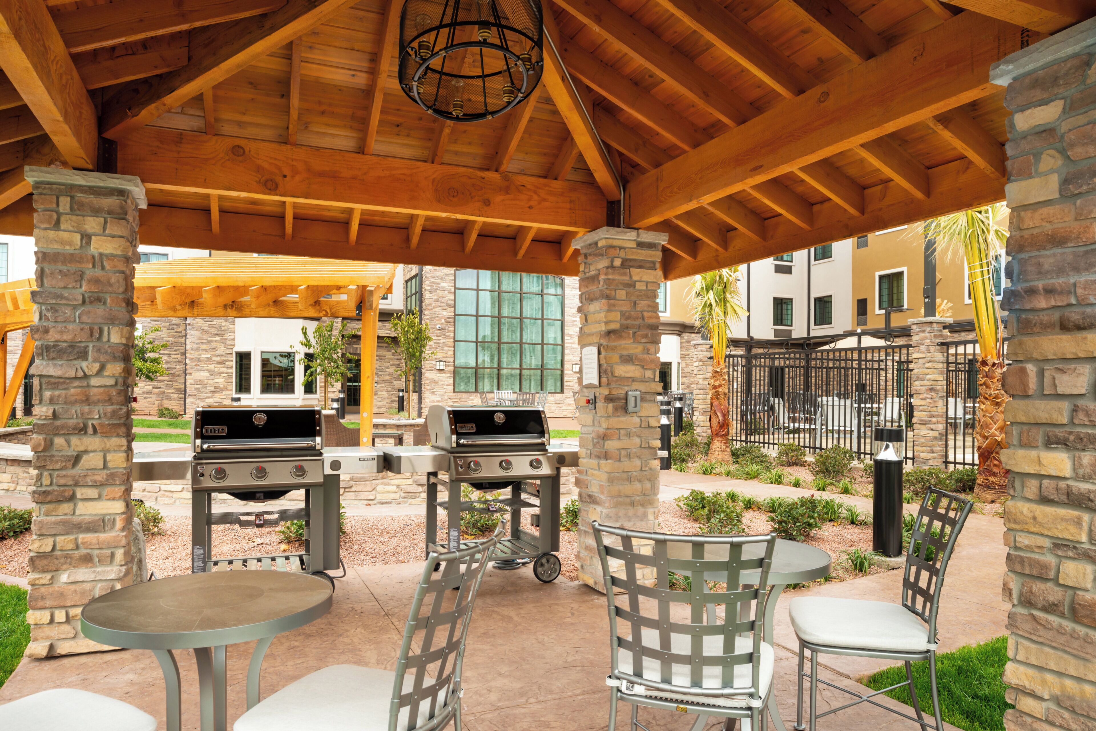 Une terrasse extérieure dotée d’un espace couvert, de piliers en pierre, d ’un coin barbecue et de sièges.