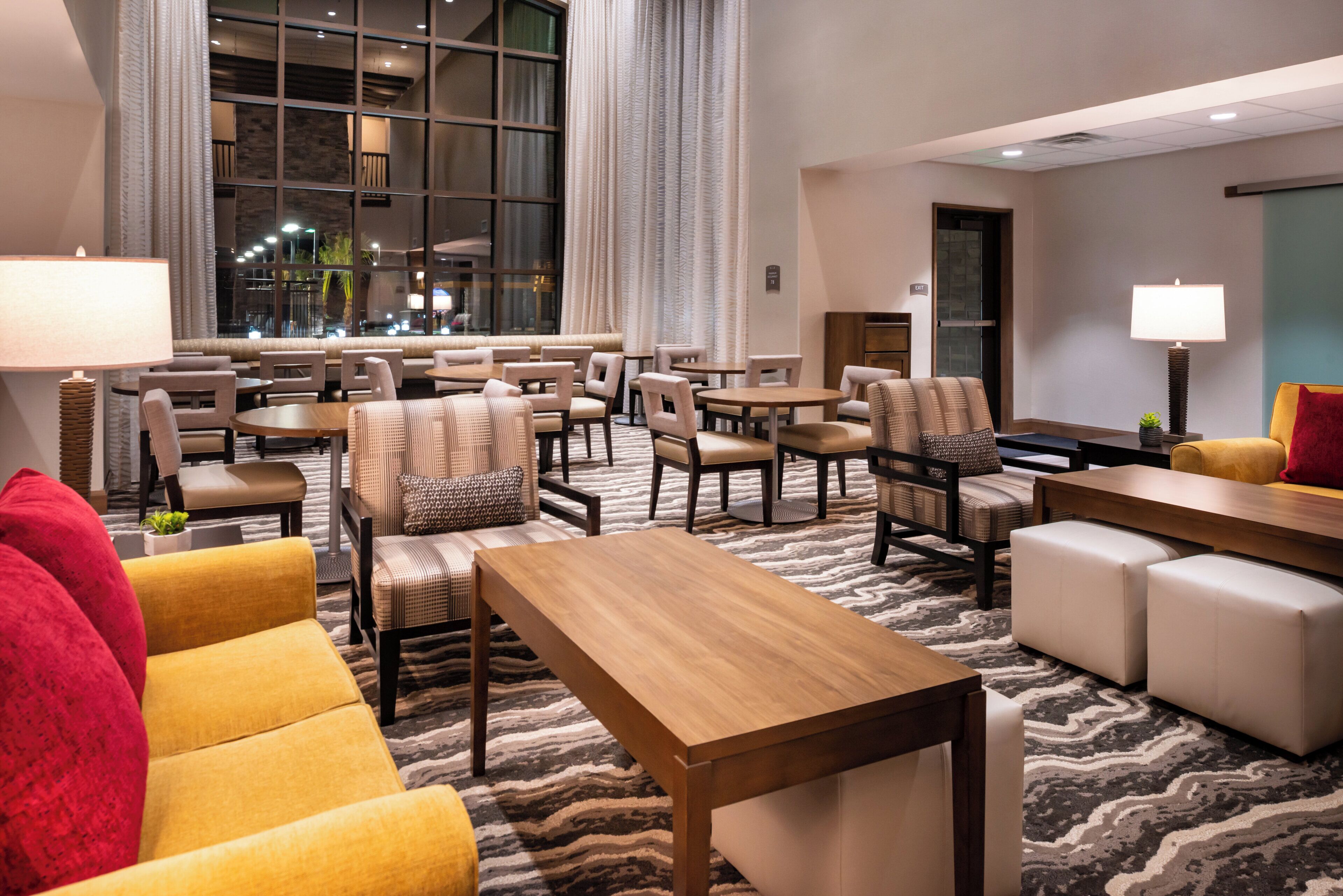 A hotel lobby with multiple seating areas, including sofas, chairs, and tables. There is a large window providing a view of the outside.