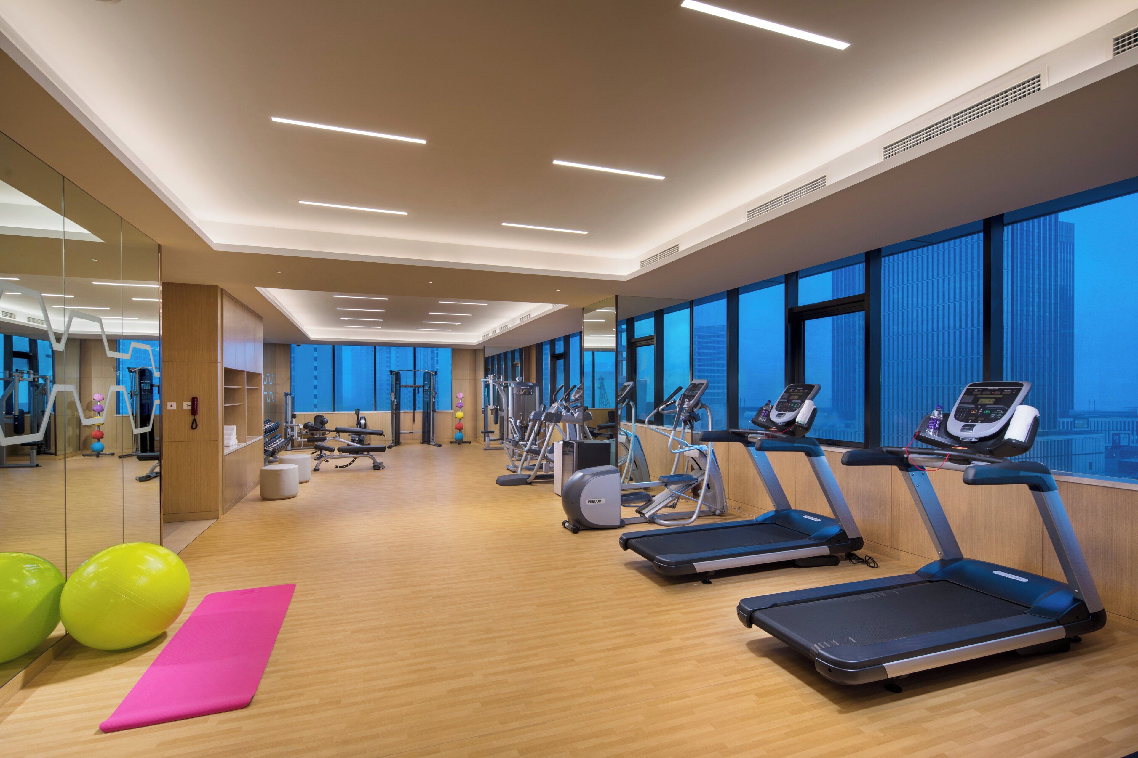 Un gimnasio moderno con equipamiento de ejercicio, ventanas amplias y suelo de madera.