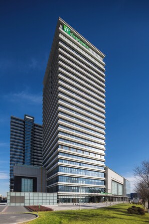 A modern hotel building with a prominent logo at the top, multiple floors, and a flat roof. - Holiday Inn Tianjin Xiqing by IHG (Tianjin)