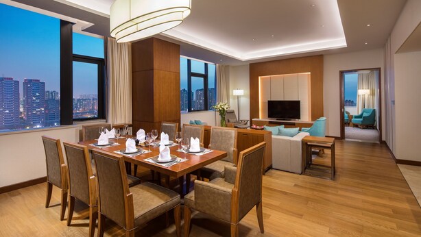 A modern hotel room with a dining area, a living room, and a large window offering a city view. - Holiday Inn Tianjin Xiqing by IHG (Tianjin)