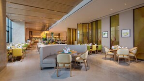 A modern dining area with round tables, cushioned seating, and a bar in the background. - Holiday Inn Tianjin Xiqing by IHG (Tianjin)
