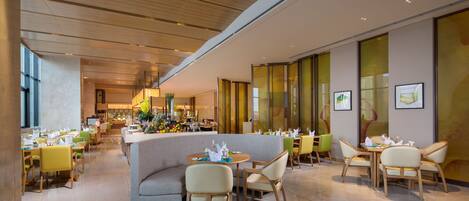 A modern dining area with round tables, cushioned seating, and a bar in the background.