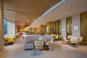 A modern dining area with round tables, cushioned seating, and a bar in the background. - Holiday Inn Tianjin Xiqing by IHG (Tianjin)