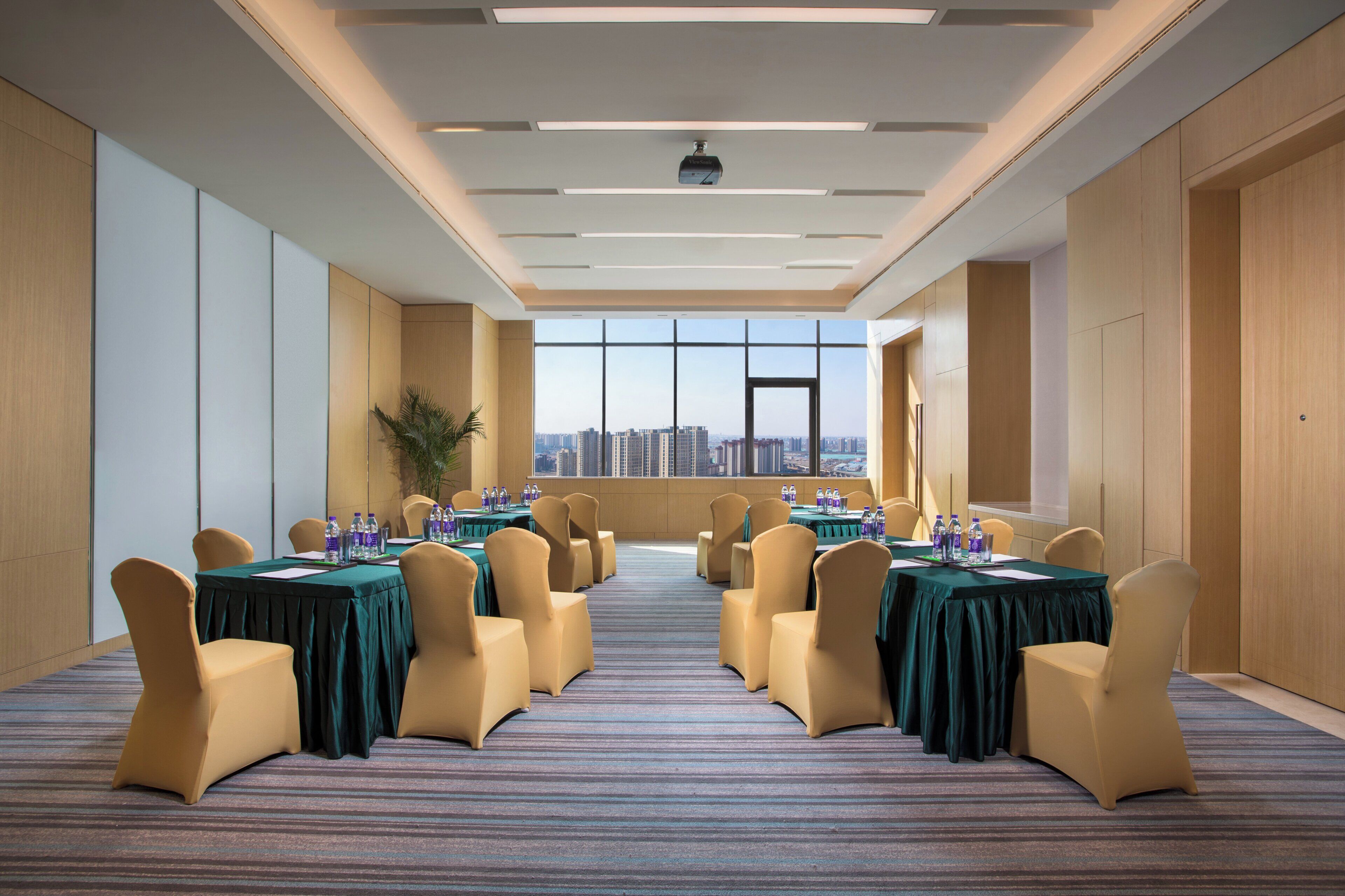 Un salón de conferencias con vistas a la ciudad, equipado con mesas, sillas y botellas de agua.
