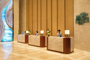 A hotel reception area with marble counters, a large abstract mural, and a Holiday Inn sign. - Holiday Inn Tianjin Xiqing by IHG (Tianjin)