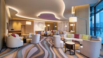 A modern hotel lobby with a central seating area, a large window offering a city view, and a ceiling with a unique light feature.
