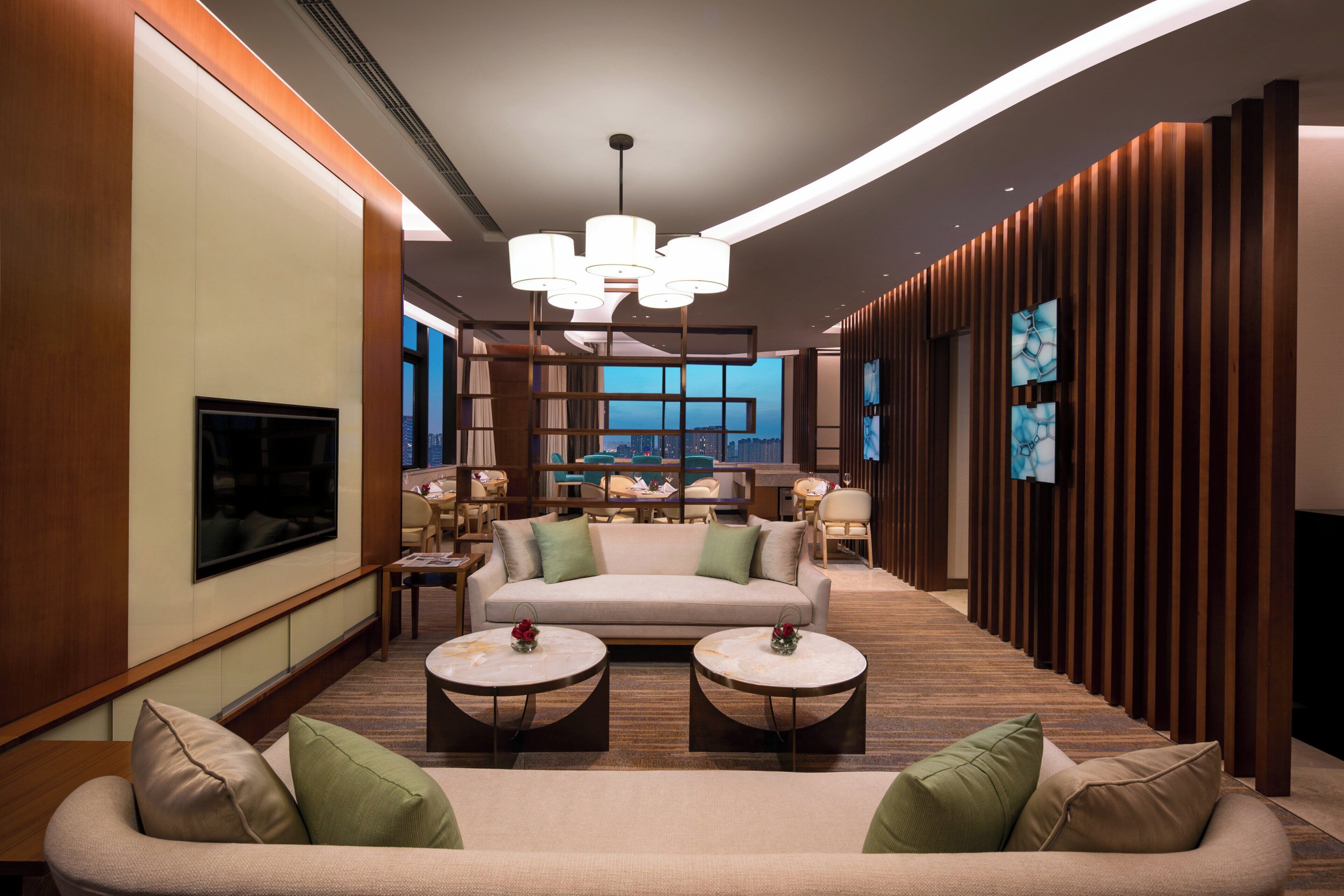 A modern hotel lobby with a sofa, two side tables, a TV, and a view of the cityscape.