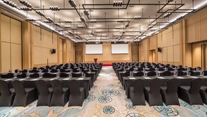 A conference room with rows of tables and chairs, a carpeted floor, and a projector screen at the front. - Holiday Inn Tianjin Xiqing by IHG (Tianjin)