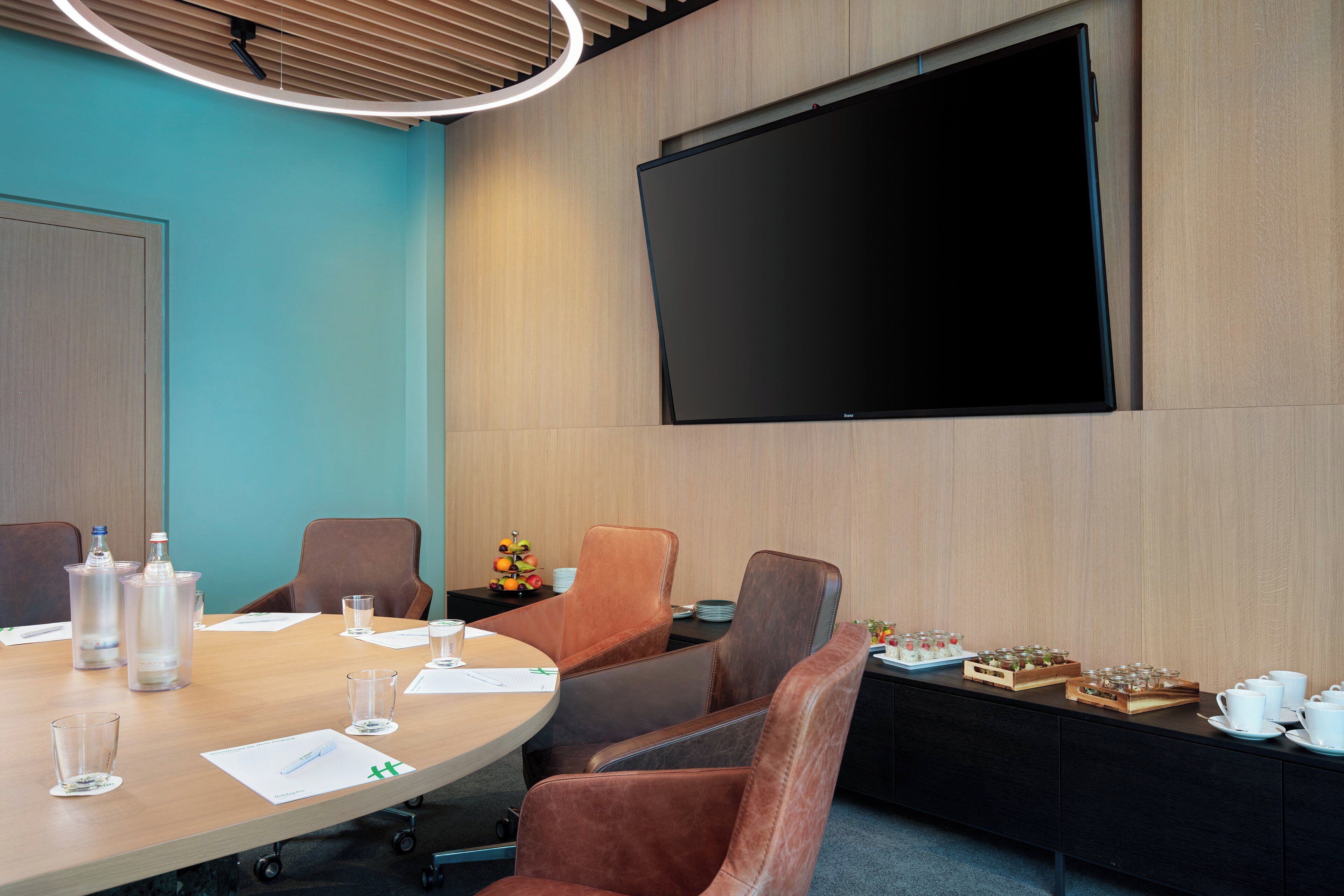 Una sala de conferencias con una gran pantalla plana, sillas de cuero, una mesa de madera y una mesa de buffet con comida y bebidas.