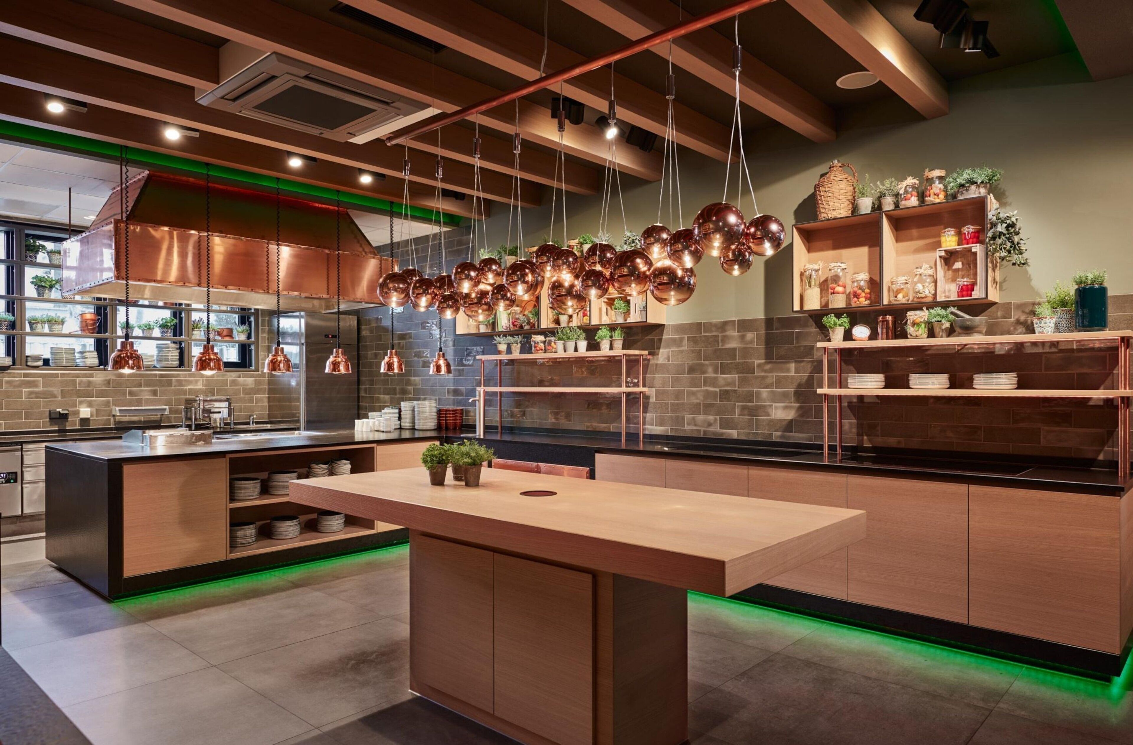 A modern kitchen with a central island, hanging copper pendant lights, and a brick backsplash.