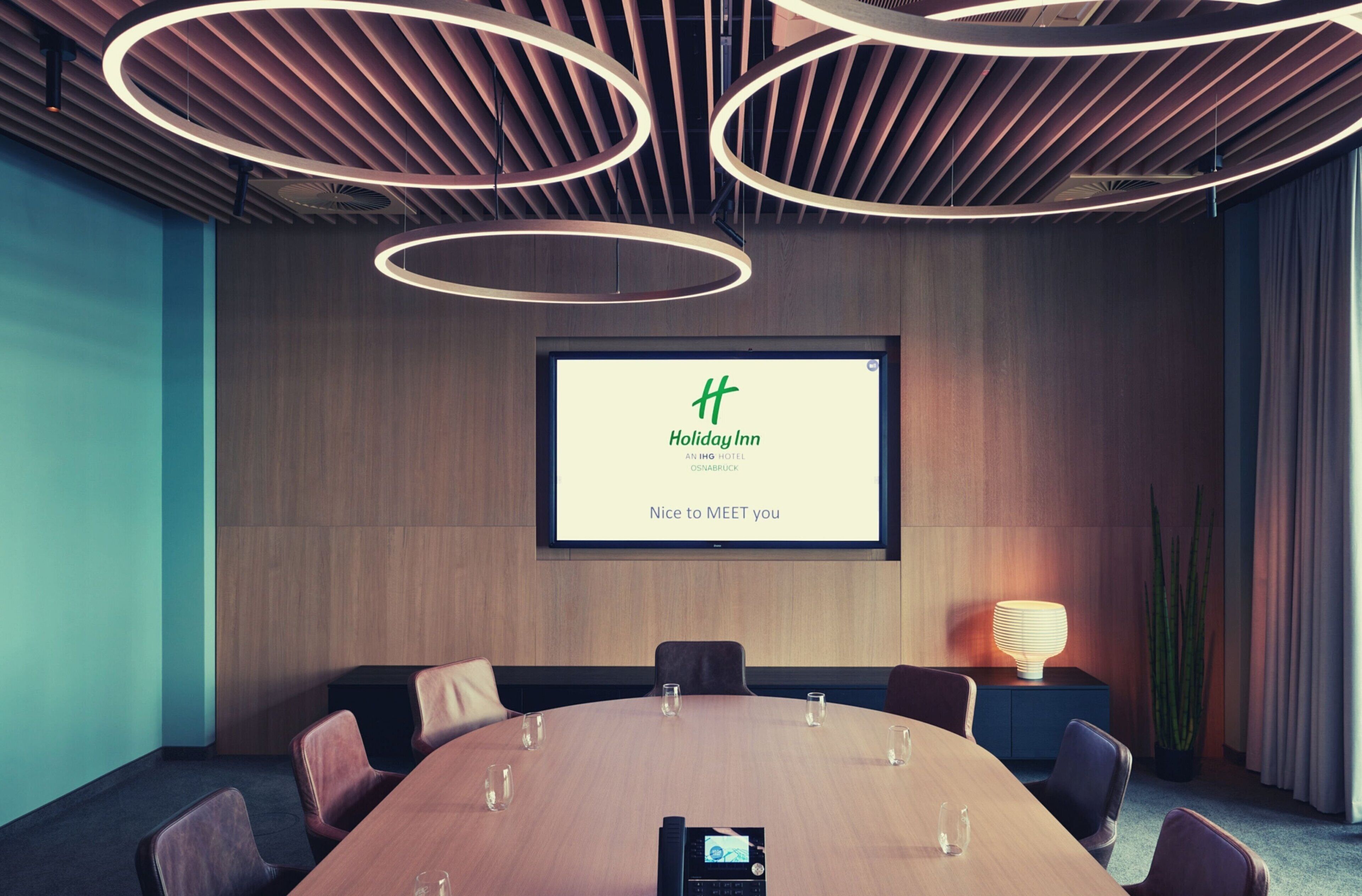 Une salle de conférence dotée d’une grande table, de chaises, d’un écran affichant le logo « Holiday Inn » et d’un design de plafond moderne.