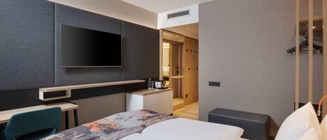 A modern hotel room with a large bed, a desk, a flat-screen TV, and a walk-in closet.