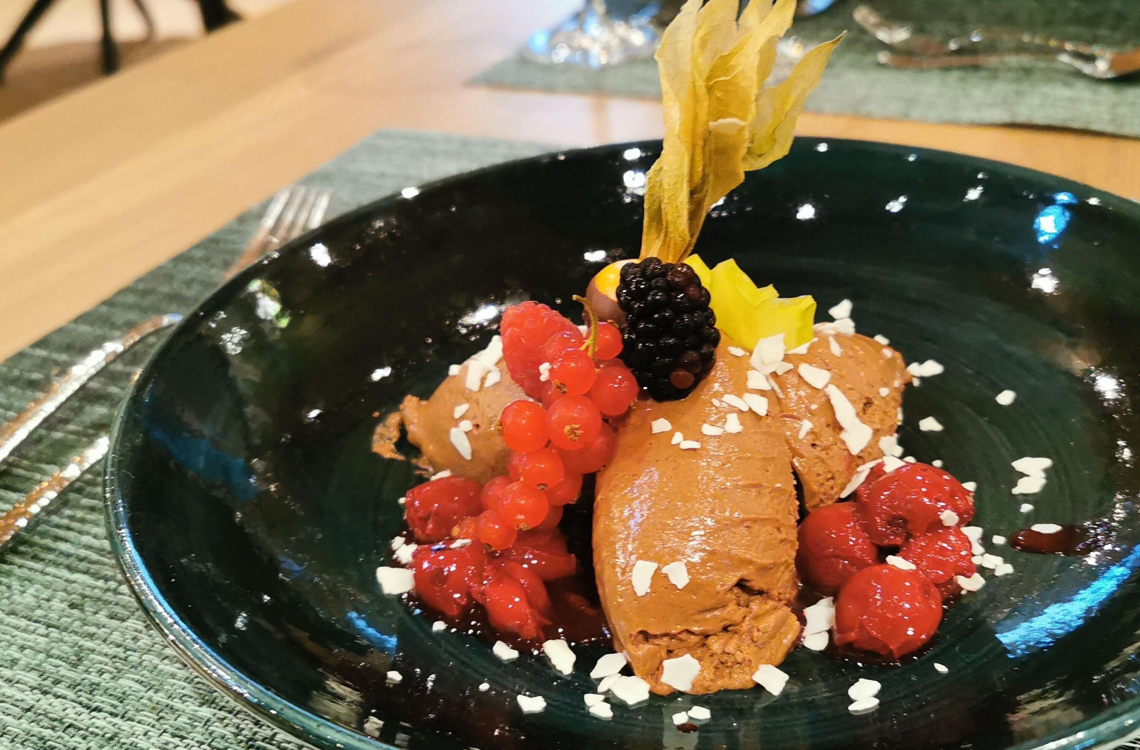A dessert on a dark plate with a garnish of fruit and a chocolate piece.