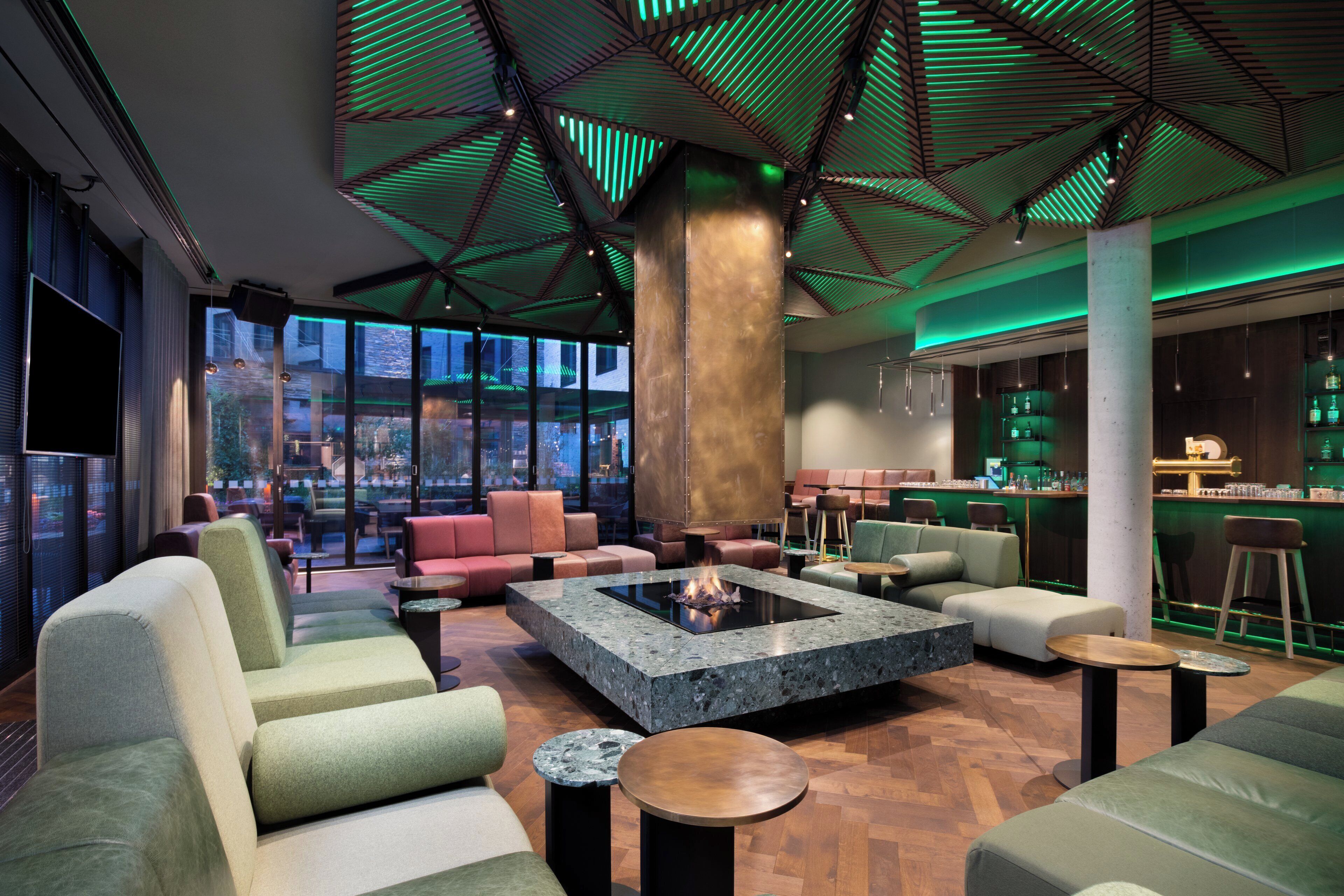 Un área de descanso moderna con asientos, una chimenea central y un bar con botellas.