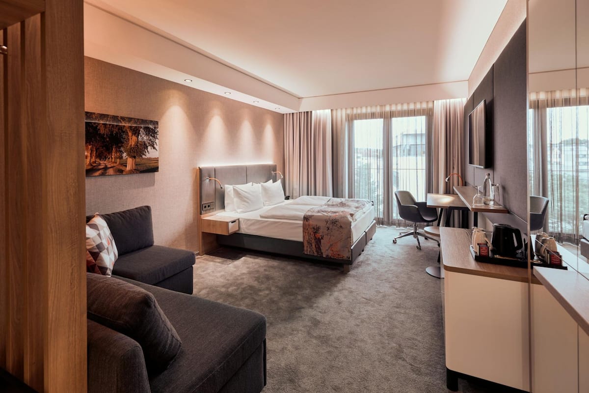 A hotel room with a bed, a desk, a chair, a sofa, and a TV.