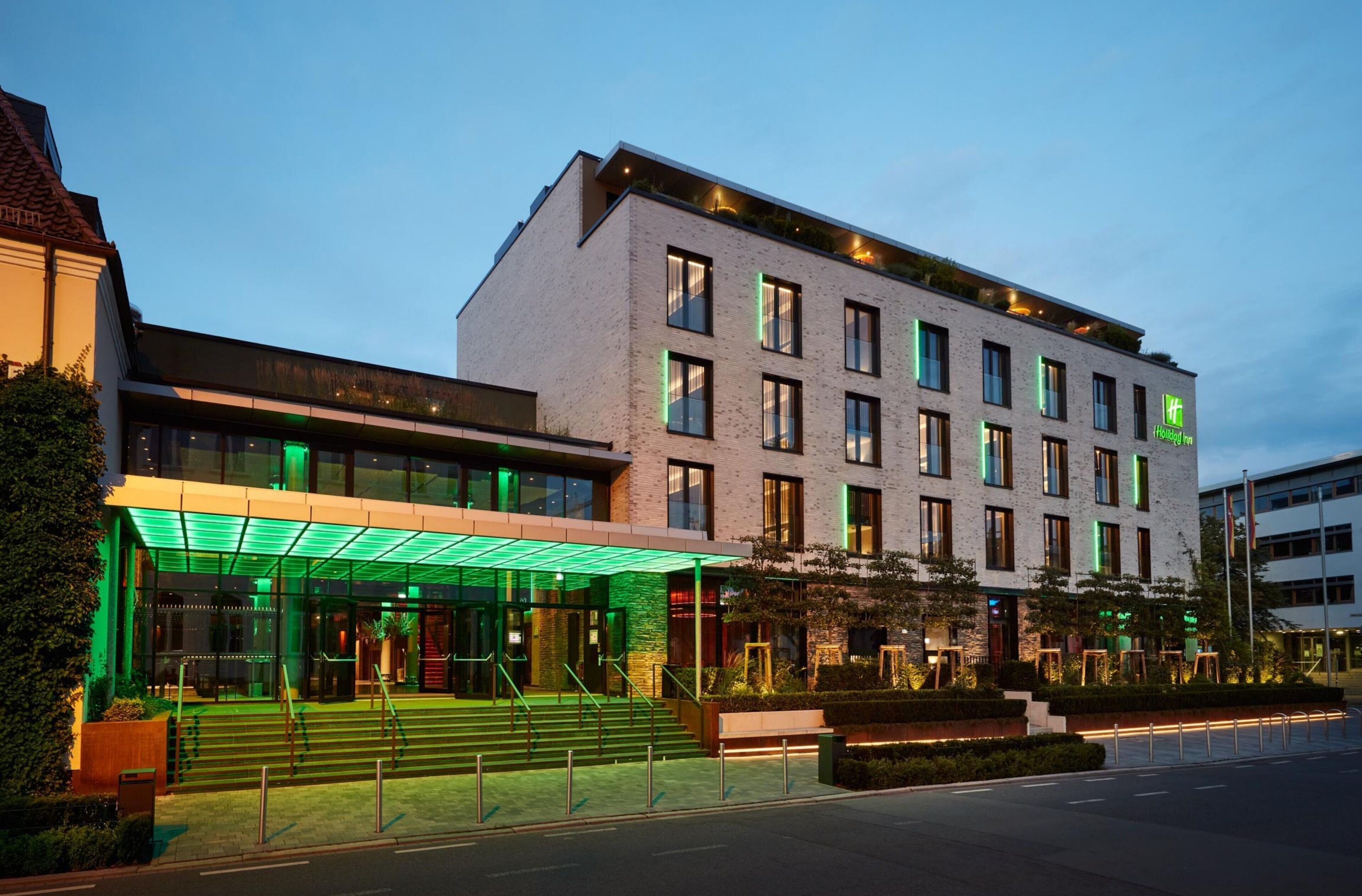 Ein modernes Hotel mit Glasfassade, Sitzgelegenheiten im Freien und einem gut beleuchteten Eingang.
