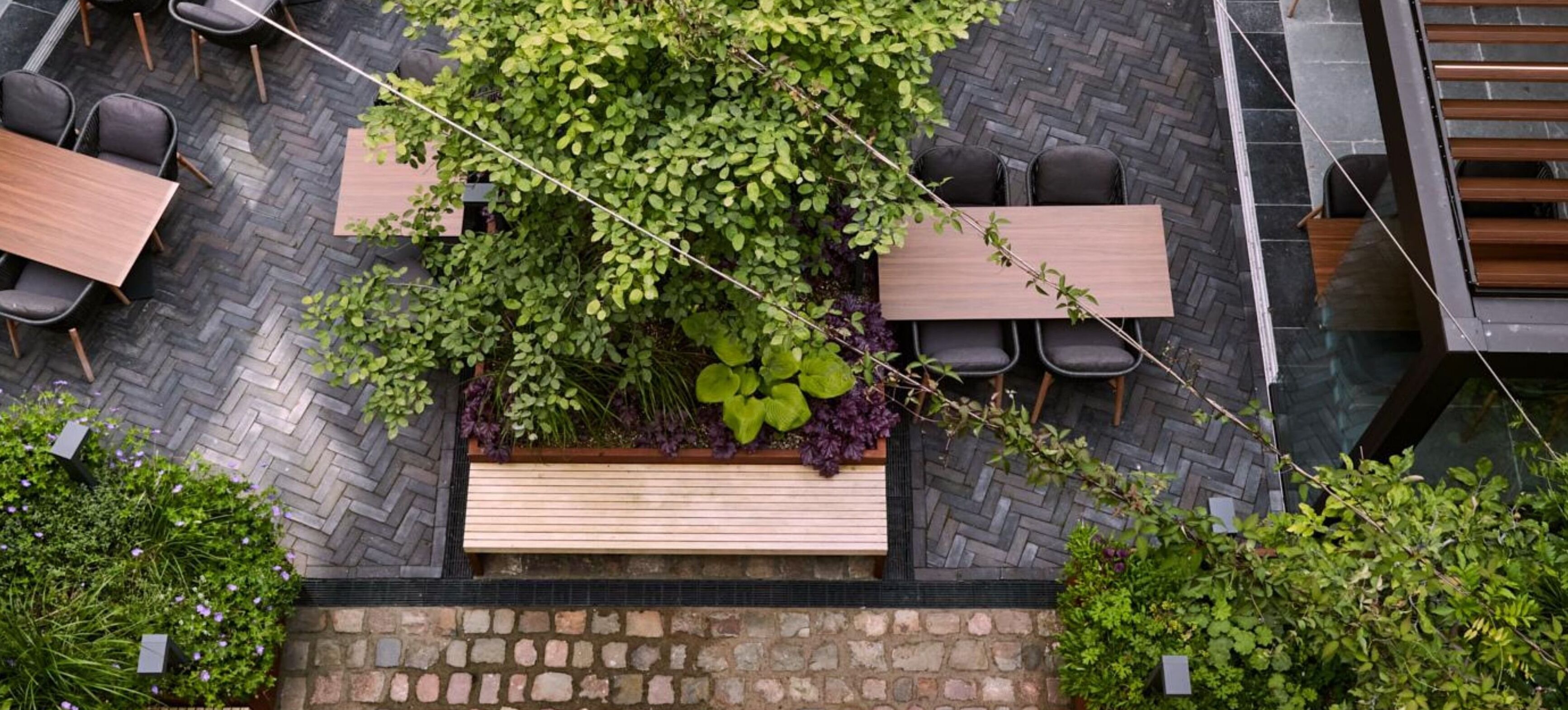 An outdoor seating area with tables and chairs, surrounded by lush greenery and a stone pathway.