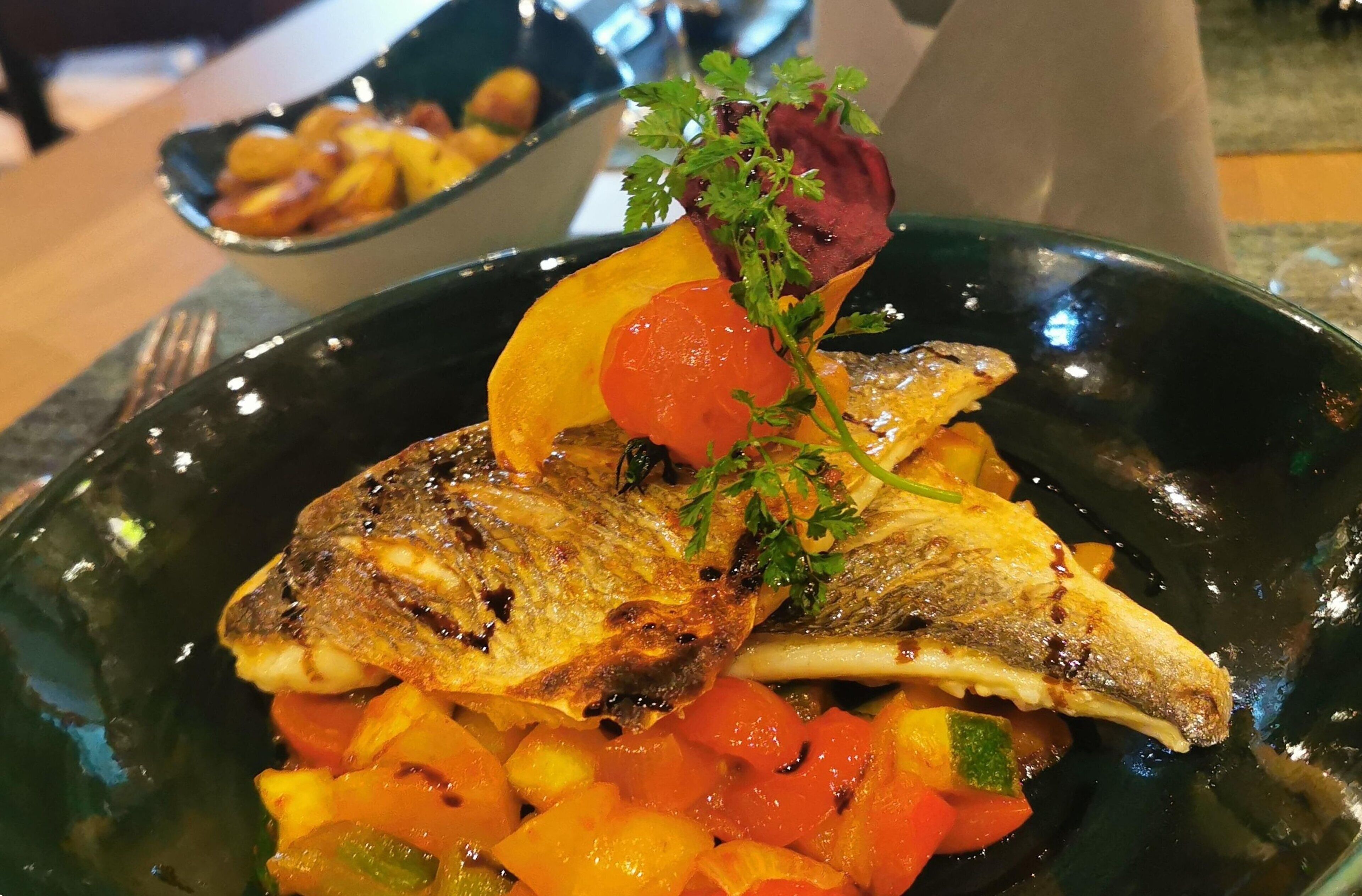 Un plato con pescado a la parrilla y verduras en un bol.