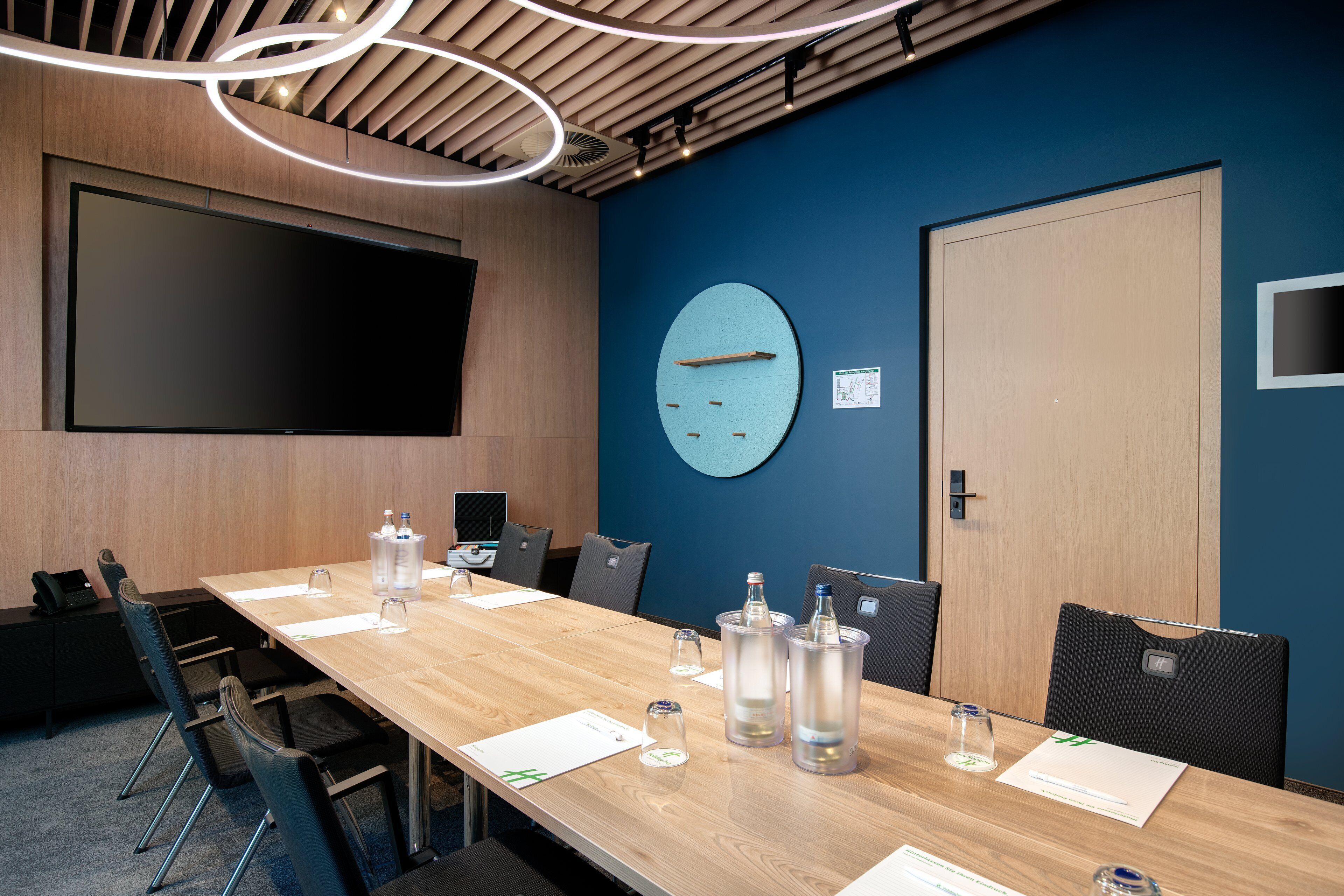Une salle de conférence avec une longue table, des chaises, une horloge et une porte.
