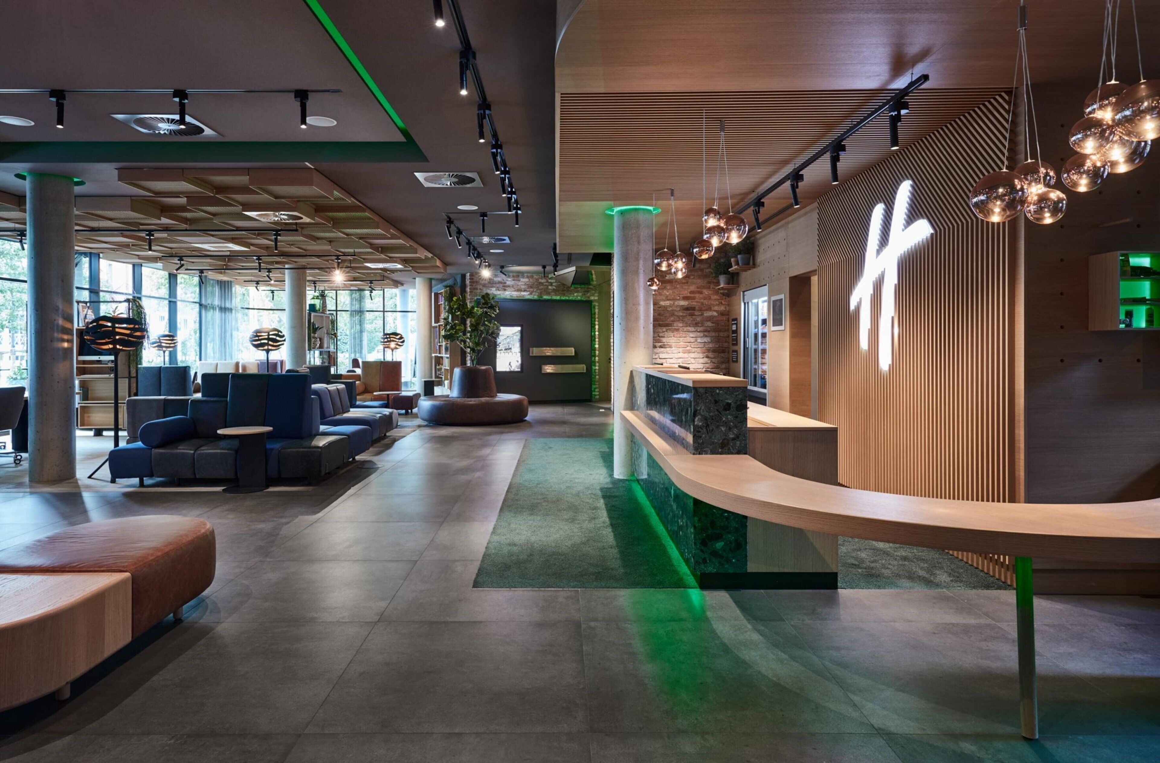 A modern hotel lobby with seating areas, a reception desk, and a large window providing natural light.