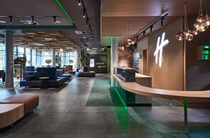 A modern hotel lobby with seating areas, a reception desk, and a large window providing natural light. - Holiday Inn Osnabrueck by IHG (Osnabrueck)