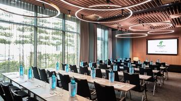 Ein Konferenzraum mit Tischen, Stühlen und einem Bildschirm, der ein Holiday Inn Logo zeigt.