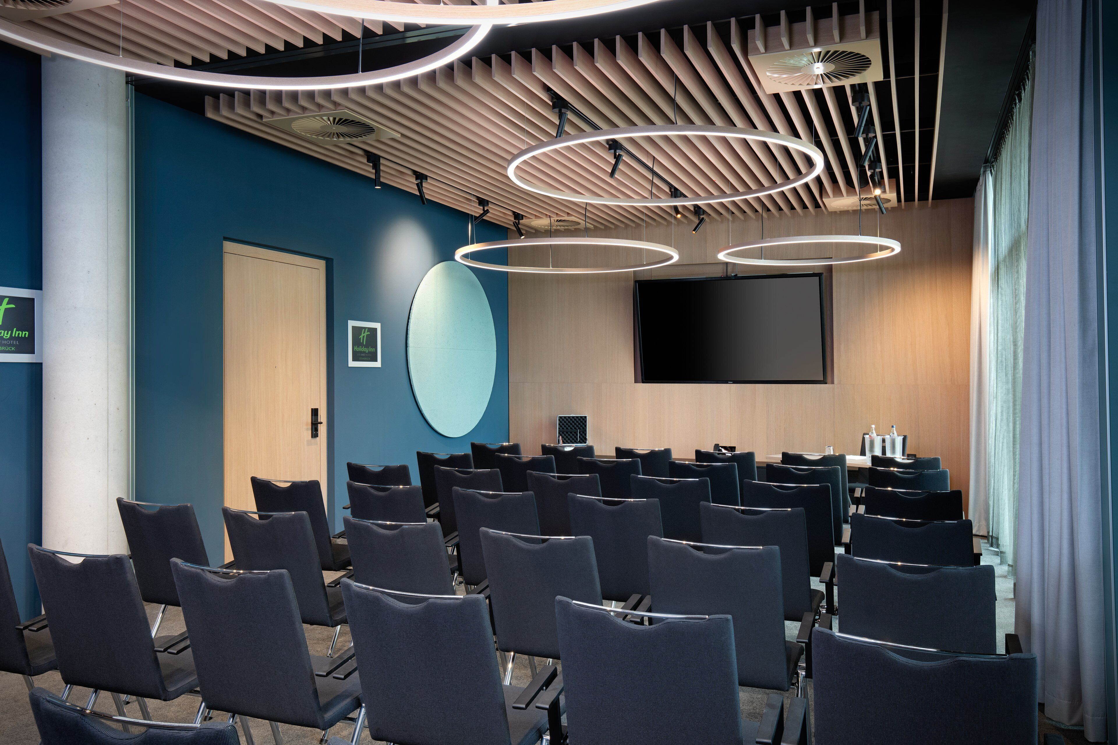 A conference room with rows of chairs, a large screen, and modern lighting fixtures.