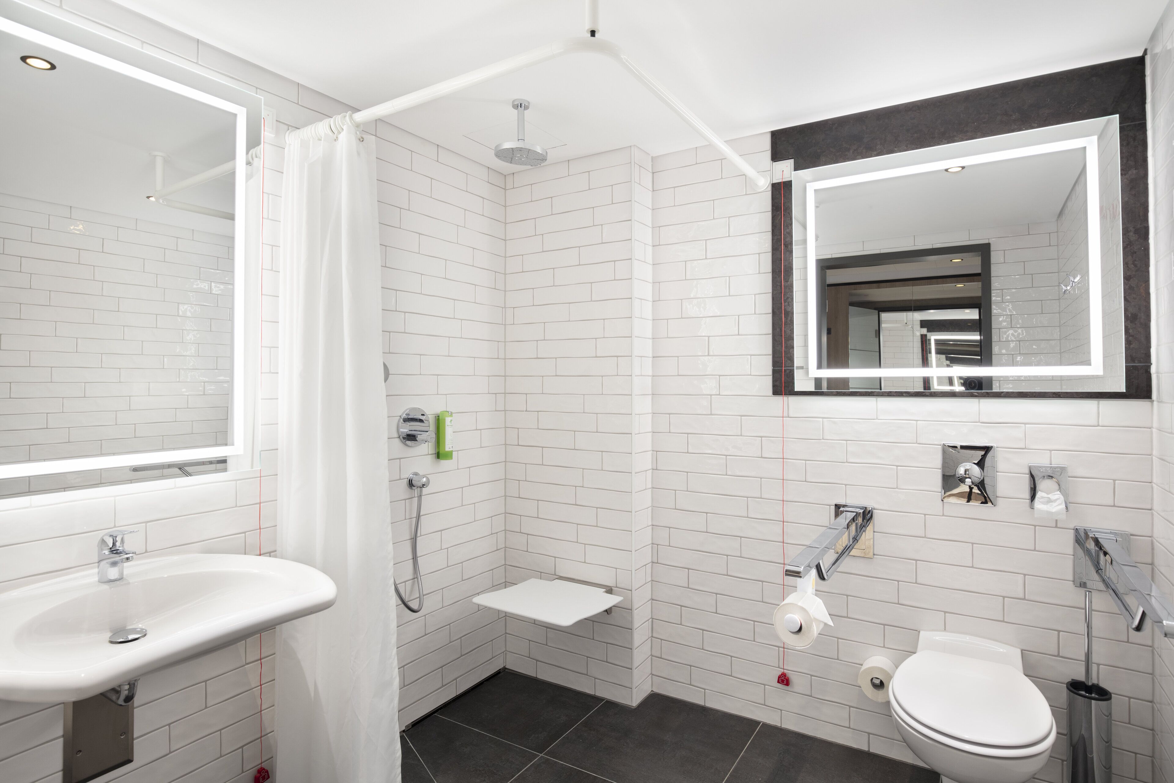 Een moderne badkamer met witte metrotegels, een witte wastafel, toilet en douche met glazen deur, plus een grote spiegel boven de wastafel.
