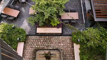 Un giardino pensile con tavoli e sedie in legno, immerso nel verde e con una fontana in pietra.
