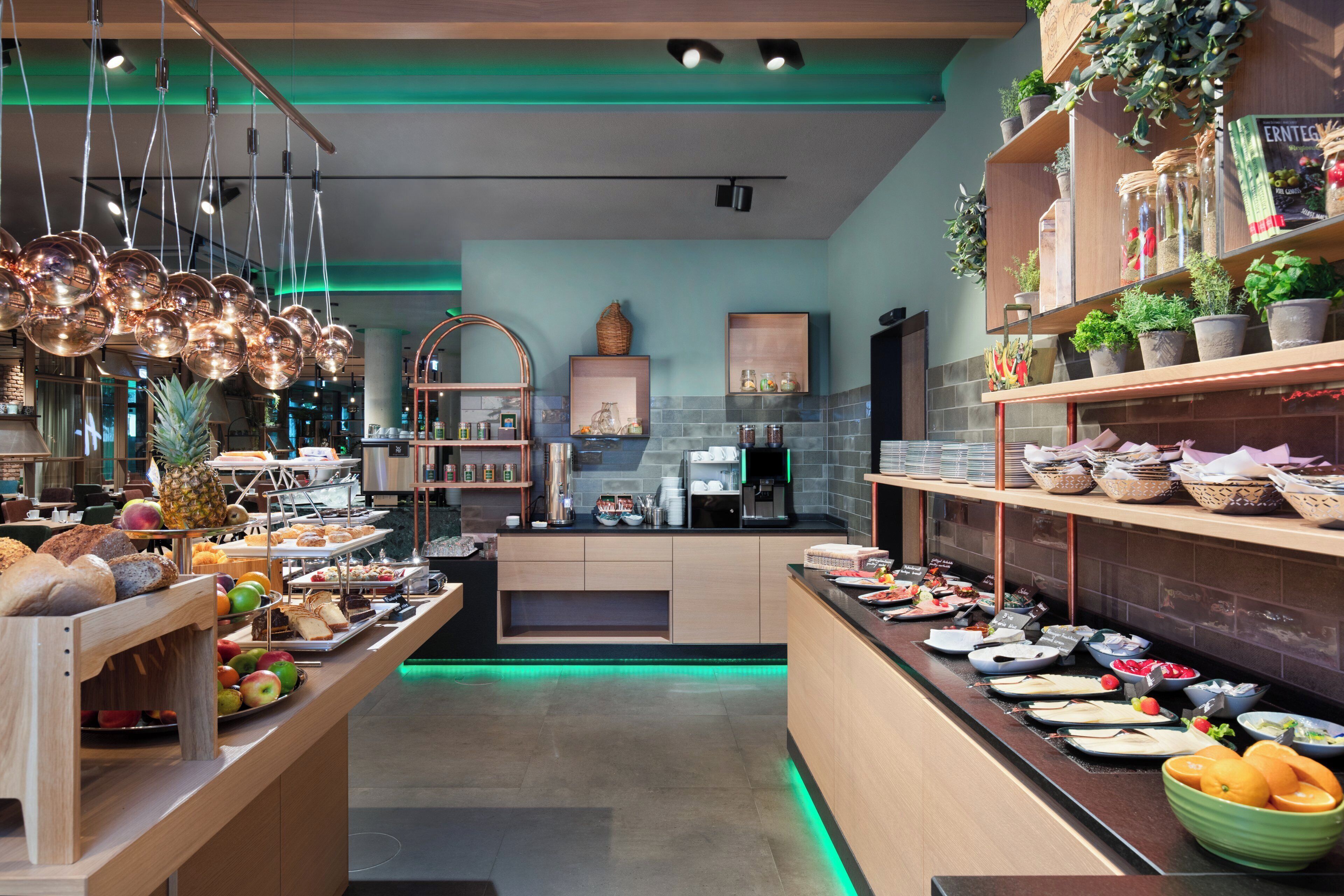 A modern café interior with a central counter, various food items, and decorative plants.